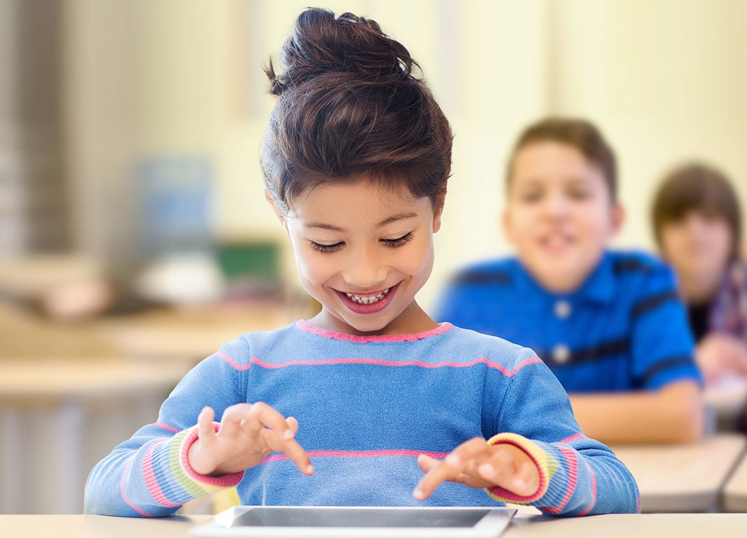 child-smiling-at-tablet-on-desk child-smiling-at-tablet-on-desk